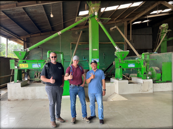 ICT team member with partners in front of hulling machinery at a dry mill in Sumatra