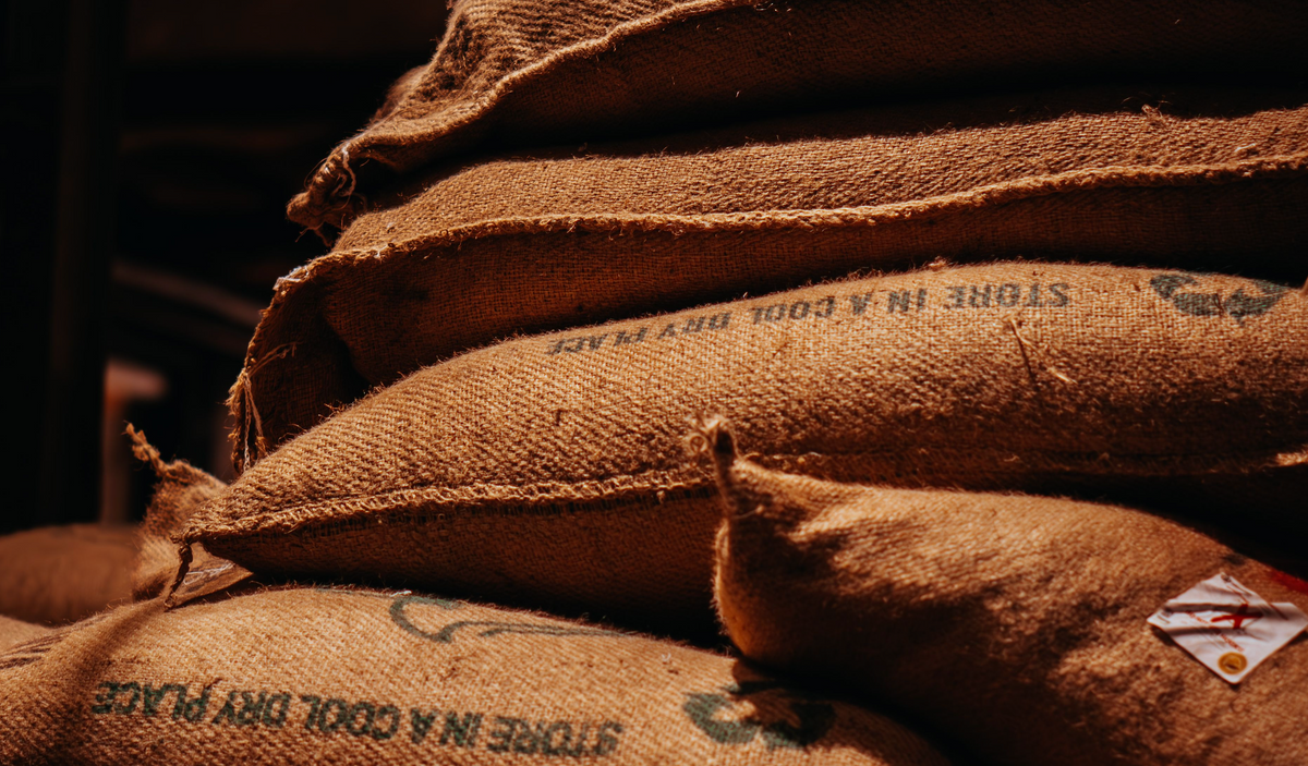 Stacked jute bags of green coffee printed with storage instructions in a dimly lit warehouse