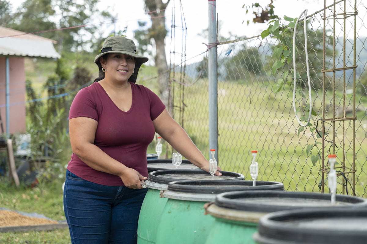 Coffee producer standing beside a row of processing barrels on her farm