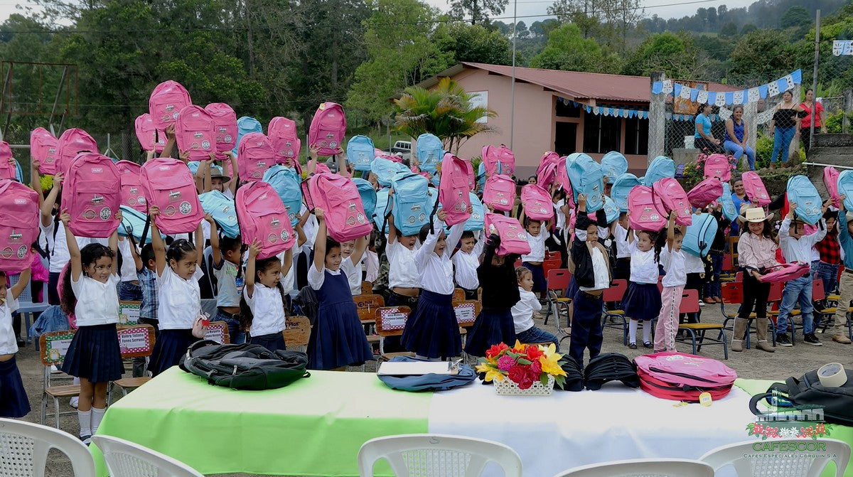 Schoolchildren in Honduras holding up new backpacks at a community school event